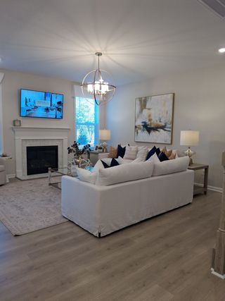 A cozy living room with a white sofa, abstract art, and a modern chandelier. Features a fireplace and wooden floors.