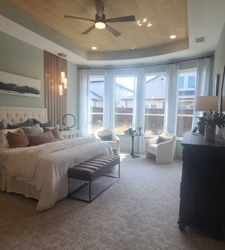 A cozy bedroom with a tufted headboard, large windows, and stylish seating area, adorned with soft, neutral tones.