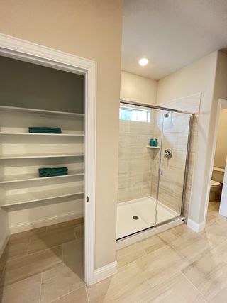 A modern bathroom with glass shower doors, beige tiles, open shelving, and recessed lighting.
