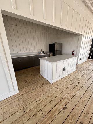 A modern kitchenette featuring rustic wood paneling, sleek countertop, and stainless appliances, set on a natural wood floor.