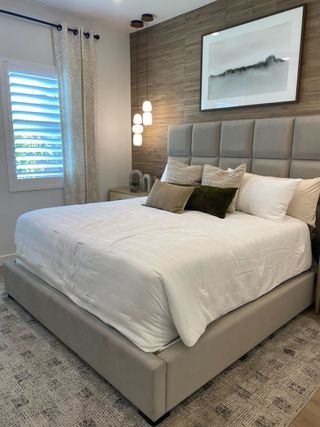 A serene bedroom features a gray upholstered platform bed with white linens, a textured accent wall, and a modern framed artwork above the headboard.