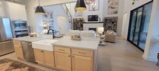 A modern open-concept living space with a sleek kitchen island, farmhouse sink, and cozy seating around a stone fireplace.