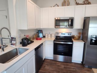 A modern kitchen with sleek stainless steel appliances, white cabinetry, and elegant wood flooring.