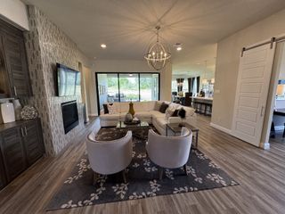 Model Home A modern living area with sleek flooring, cozy seating, and a chic chandelier, opening to a bright patio view.