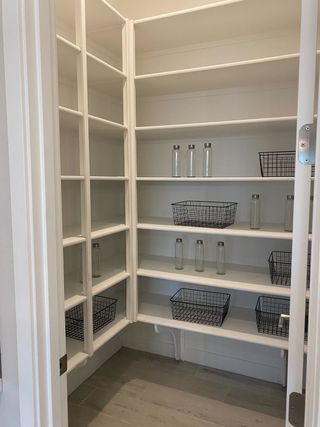 A well-organized pantry features white built-in shelving with glass jars and black wire baskets, offering ample storage space for kitchen essentials.