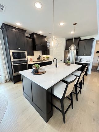 A modern kitchen with sleek black cabinets, a large island, and stylish pendant lighting.