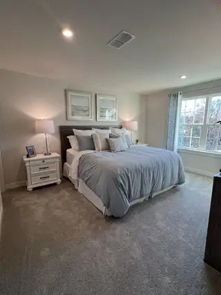 Model Home A cozy bedroom featuring plush carpeting, elegant bedding, and soft lighting for a serene ambiance.