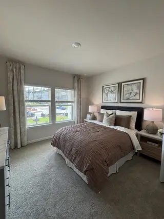Model Home A cozy bedroom featuring a plush bed, soft lighting, and elegant decor with framed artwork above the headboard.