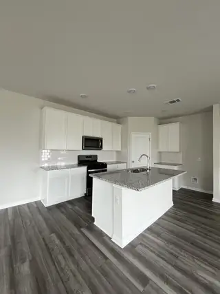 Model Home A modern kitchen with granite countertops, white cabinetry, a large island, and stainless steel appliances.
