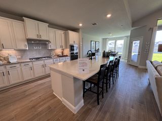 Model Home A spacious kitchen with white cabinets, an expansive island, and modern appliances, opening to a bright dining area.