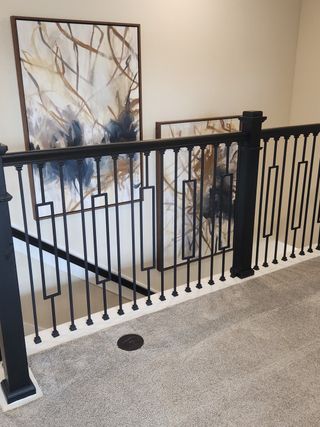 A chic upstairs hallway featuring abstract artwork and elegant black railings on plush carpet.