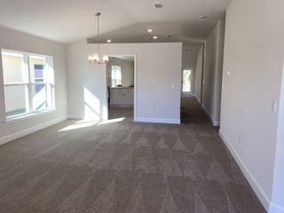 A bright, carpeted living area with a modern chandelier, neutral walls, and an open entry to the kitchen.