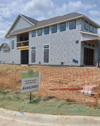 A modern home under construction in The Grove Frisco by Chesmar Homes, featuring a spacious design and large windows (Frisco, TX).