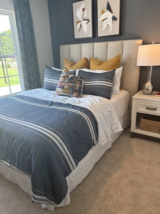 Model Home A cozy bedroom with a tufted headboard, abstract art, and a stylish striped bedding set illuminated by natural light.