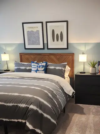 A cozy bedroom with a wood headboard, stylish bedding, dual nightstands, and modern framed artwork.