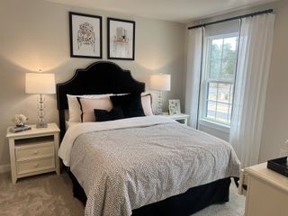 A cozy bedroom featuring a plush bed with patterned bedding, elegant lamps, and chic wall art, bathed in natural light.
