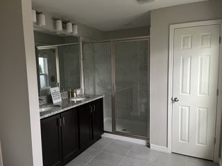 Model Home A modern bathroom featuring a granite countertop, dark wood vanity, and elegant glass shower enclosure.