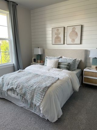 A cozy bedroom with shiplap walls, soft bedding, elegant lamps, and abstract wall art for a serene ambiance.