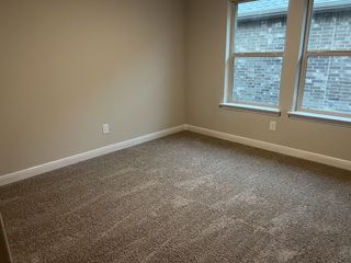 A cozy, carpeted room with neutral walls and two large windows for natural light.
