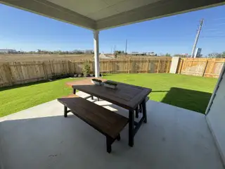 Model Home A cozy covered patio with a wooden picnic table overlooking a lush green backyard.