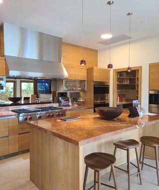 A modern kitchen featuring a marble countertop island, high-end appliances, wood cabinetry, and stylish pendant lights.