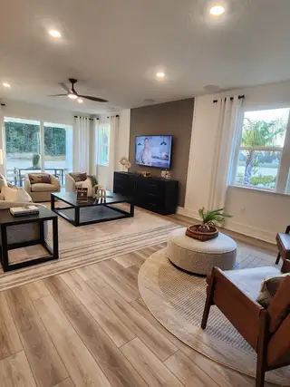 A spacious living room with large windows, natural light, and a cozy neutral-toned design.
