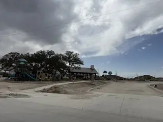 A playground and pavilion in Riverstone at Westpointe by D.R. Horton, set against a cloudy sky, in San Antonio, TX.