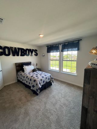 A cozy bedroom with plush carpeting, sports-themed decor, and bright natural light from large windows.