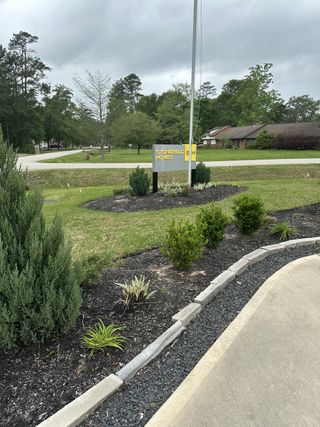 Lush greenery surrounds a charming community entrance in Roman Forest by Stonefield Homes, New Caney, TX.