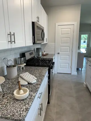A modern kitchen with granite countertops, stainless steel appliances, and white cabinetry.