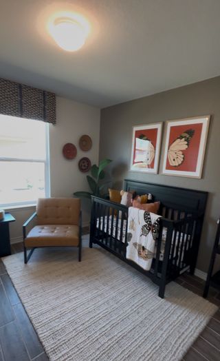 A stylish nursery in The Granary home, featuring a black crib, a tan leather armchair, framed butterfly artwork, and a light-colored rug on dark tile flooring (San Antonio, TX).
