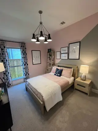 Model Home A cozy bedroom with soft pink walls, modern lighting, and stylish decor, featuring a comfortable bed and nightstand.