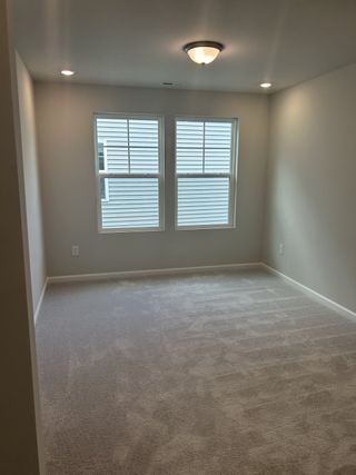 A spacious bedroom with plush carpeting and natural light streaming through double windows for a cozy retreat.