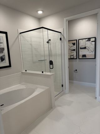 A modern bathroom with a glass shower, a cozy bathtub, and chic black and white wall art.