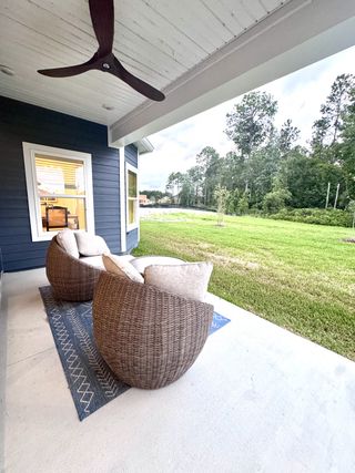 A cozy patio with wicker chairs, a fan, and a serene view of nature.