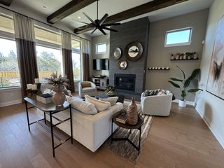 A modern living room featuring a cozy fireplace, beamed ceiling, and large windows with stylish decor and neutral tones.