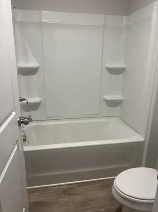 A sleek bathroom with a minimalist white tub, elegant shelving, and wood-look flooring.