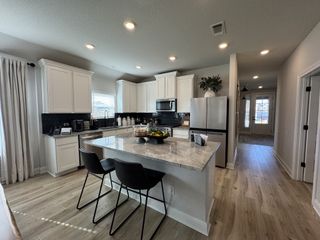 Model Home A modern kitchen with white cabinetry, granite countertops, and sleek appliances, accented by warm wood flooring.