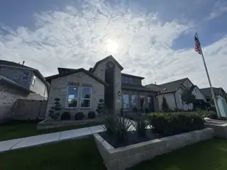 Street view A charming stone-front home with manicured landscaping in Nolina 50s by Taylor Morrison (Georgetown, TX).
