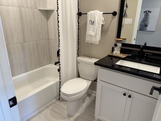 A chic bathroom design featuring a white vanity with black hardware, a black-framed mirror, and a shower/tub combination with elegant tile work.