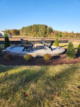 A serene outdoor fire pit with Adirondack chairs and lush greenery in Grove At Gin Branch by Mattamy Homes (Wendell, NC).