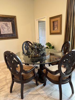 Model Home An elegant dining area with a glass-top table, ornate chairs, and classic wall art, offering a cozy, refined setting.