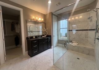 Model Home A luxurious bathroom with a sleek dark vanity, large glass shower, and elegant marble flooring.