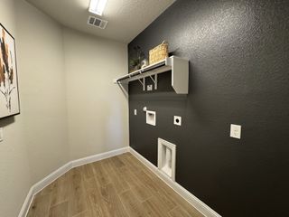 A modern laundry room with dark accent walls, wood-style flooring, and white storage shelves.