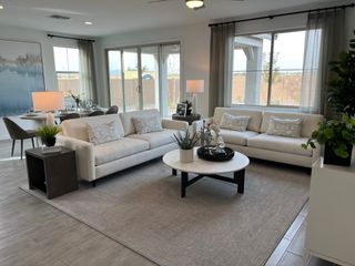 A modern living room with sleek sofas, large windows, and a cozy dining area, filled with natural light and stylish decor.