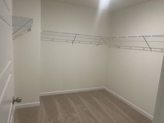 A spacious walk-in closet with neutral walls, carpet flooring, and white wire shelving for organized storage.
