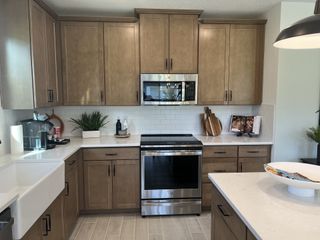 Model Home A modern kitchen with wooden cabinets, stainless steel appliances, and sleek white countertops.
