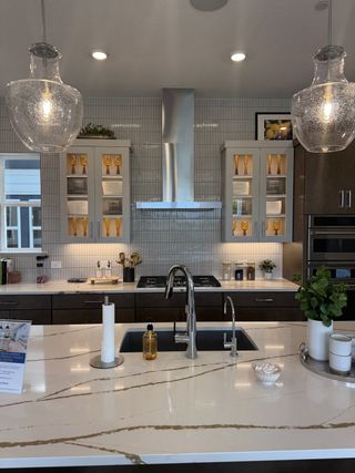 A modern kitchen with sleek cabinetry, glass pendant lights, and a marble island featuring a stainless steel sink.