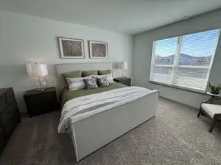 A bright bedroom boasts plush carpeting, natural light, and a stylish upholstered bed, creating a comfortable and inviting retreat.