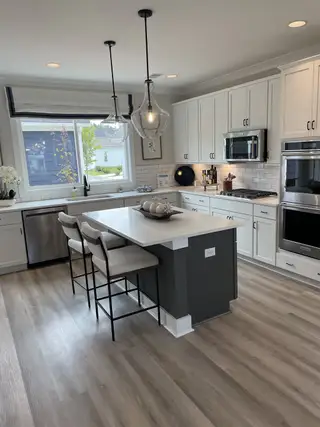 Model Home A modern kitchen with white cabinetry, a sleek island, pendant lighting, and light wood flooring.